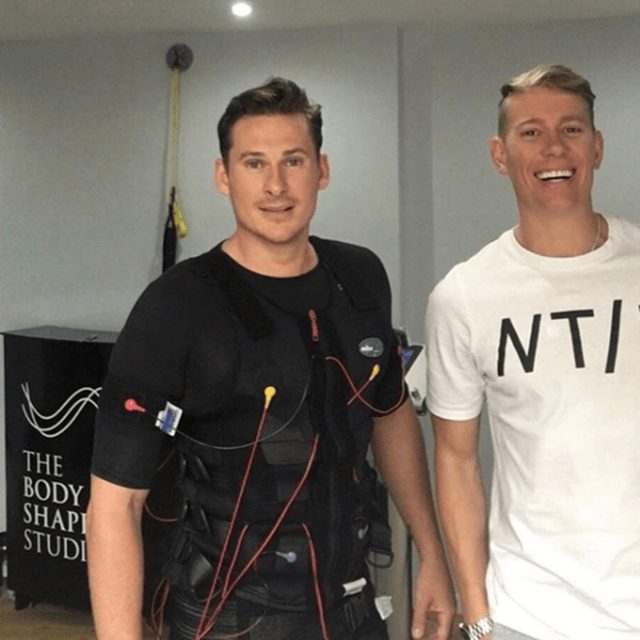 A man wearing a wired EMS training suit standing beside his trainer