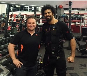 Trainer standing beside a client wearing an EMS suit in a gym